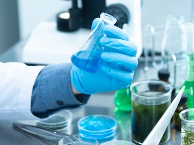 Un technicien de laboratoire dans un laboratoire tenant un bécher de liquide bleu.